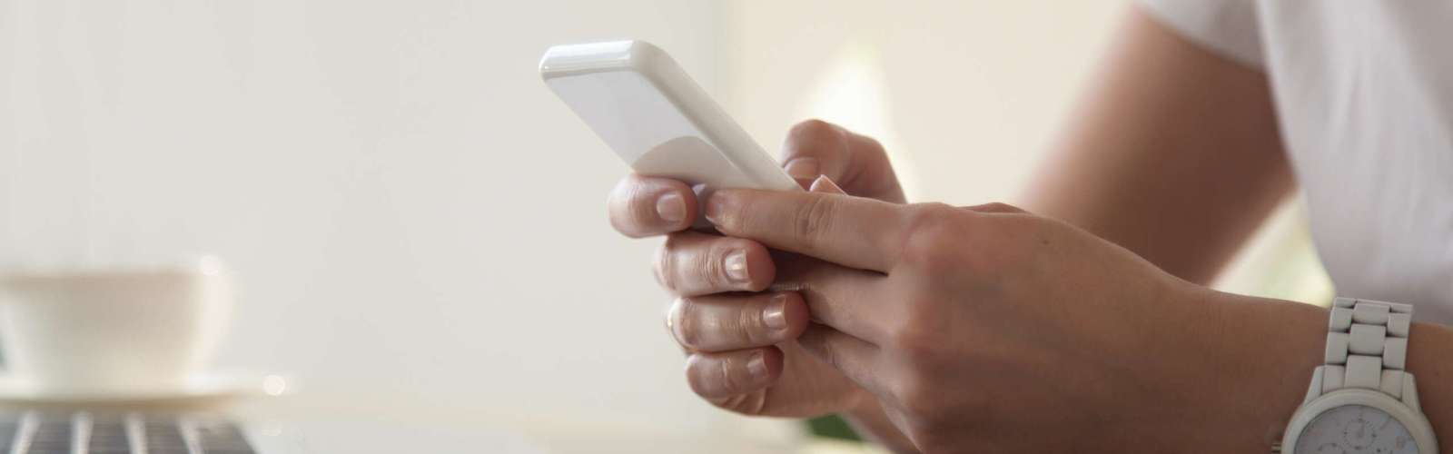 Close up image of modern cellphone in womans hand at desk with laptop. Office worker boring at workplace and playing games, writing in social networks. Businesswoman looking important contact on phone
